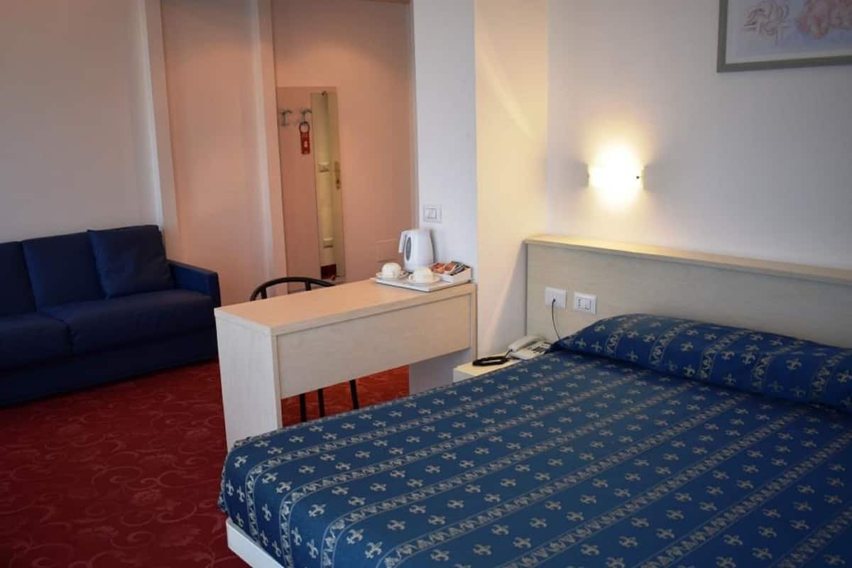 A hotel room with a bed, a desk, a chair, and a sofa.