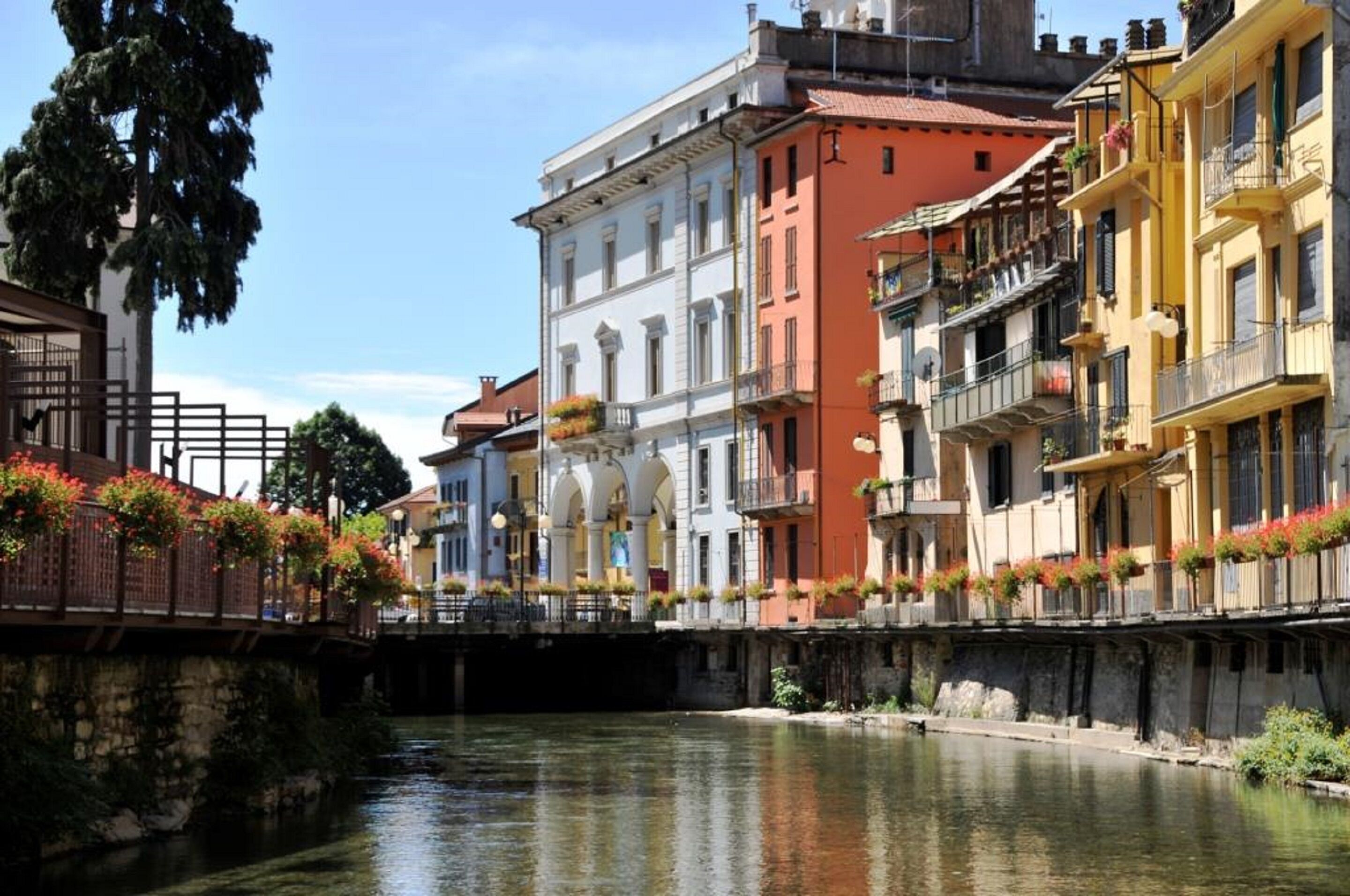 A canal with buildings on either side, featuring balconies with flower boxes and a bridge in the foreground.