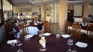 Un comedor con mesas redondas preparadas para el servicio, sillas y una zona de bar al fondo.