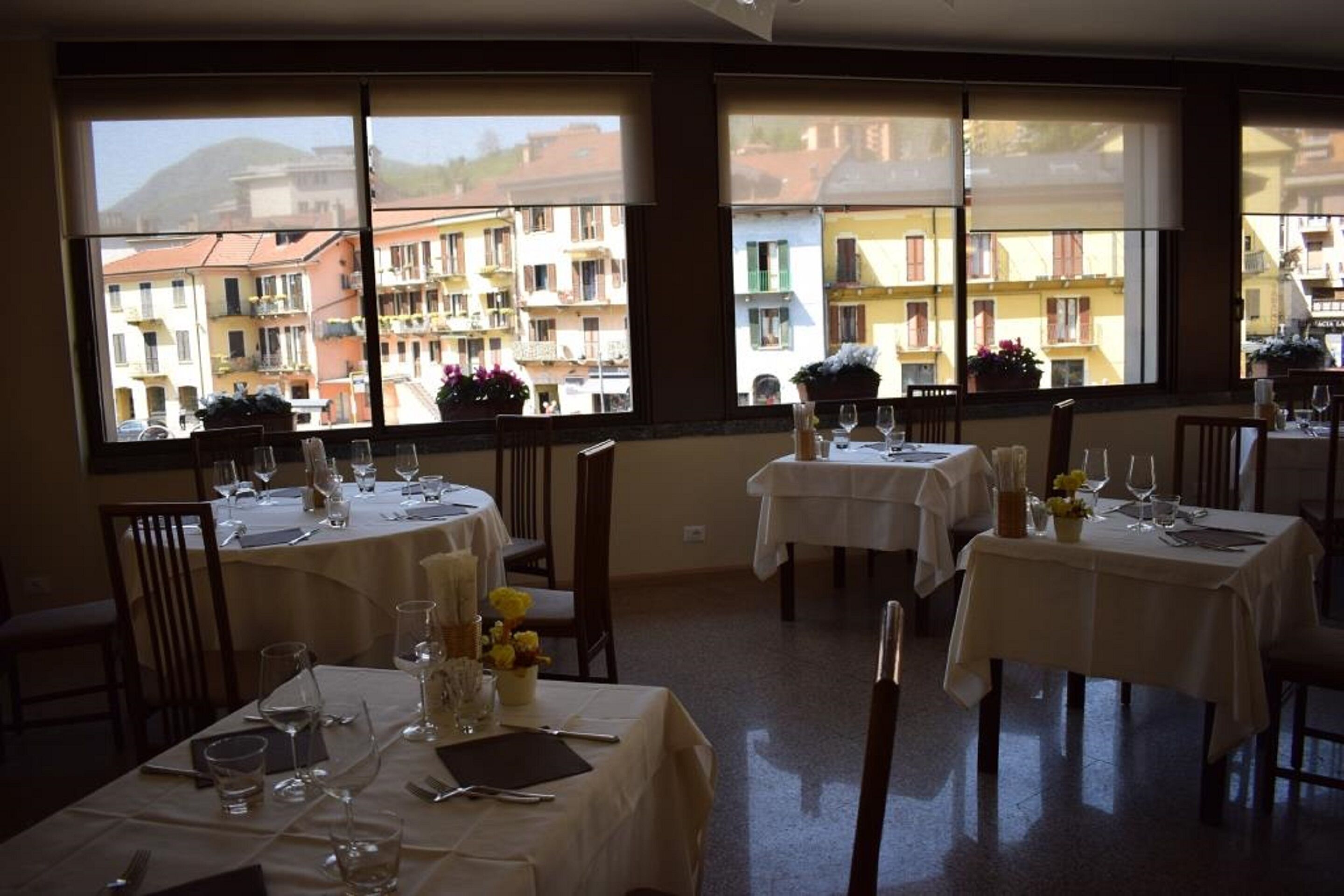 A restaurant with tables set for dining, large windows with a view of buildings, and a clean, organized interior.