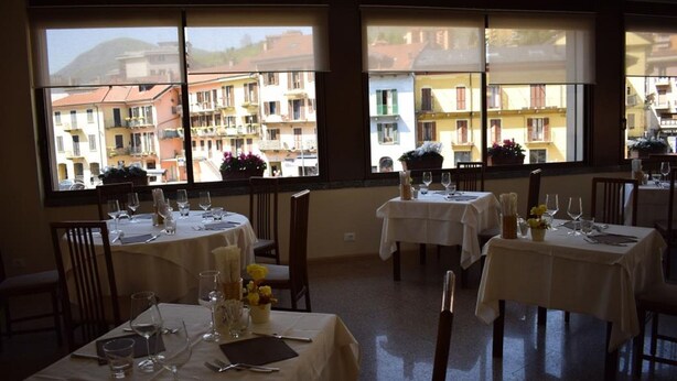 A restaurant with tables set for dining, large windows with a view of buildings, and a clean, organized interior. - Croce Bianca (Omegna)