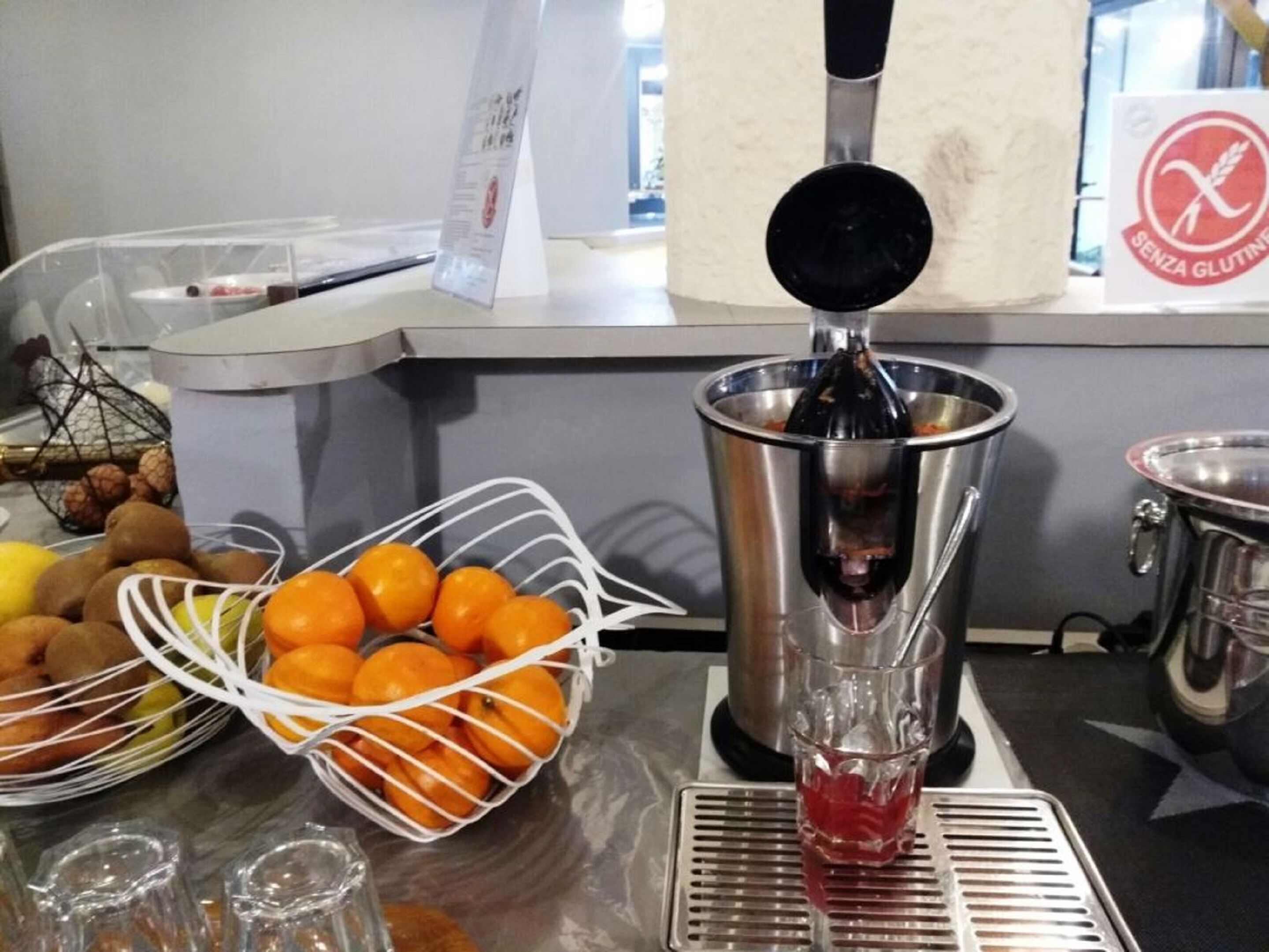 A kitchen counter with a juicer, a basket of oranges, and a bowl of fruits.