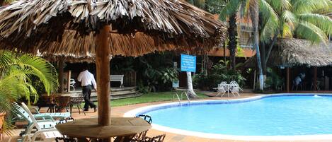 Un área de piscina con una sombrilla de paja, sillas de descanso y un letrero que indica un restaurante.