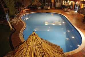 An indoor swimming pool with a thatched roof structure, surrounded by lounge chairs and tables. - Gran Hotel Paris (La Ceiba)