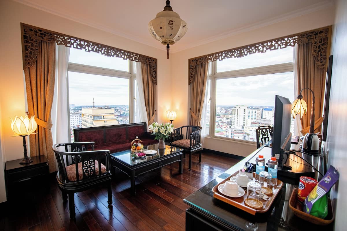 A hotel room with a city view, a sofa, a dining table with a tray of breakfast items, and a television.