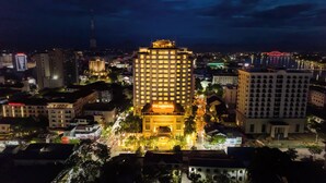 Un grand hôtel, reconnaissable à son enseigne imposante, entouré d’autres immeubles et bordé d’une rue animée la nuit.