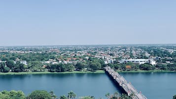 Vista panoramica di una città con un ponte imponente su un vasto specchio d'acqua, circondata da vegetazione e edifici residenziali.