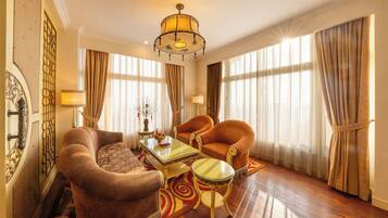 Une chambre d’hôtel avec un plancher en bois, un canapé, deux fauteuils, une table basse en verre et un lustre.