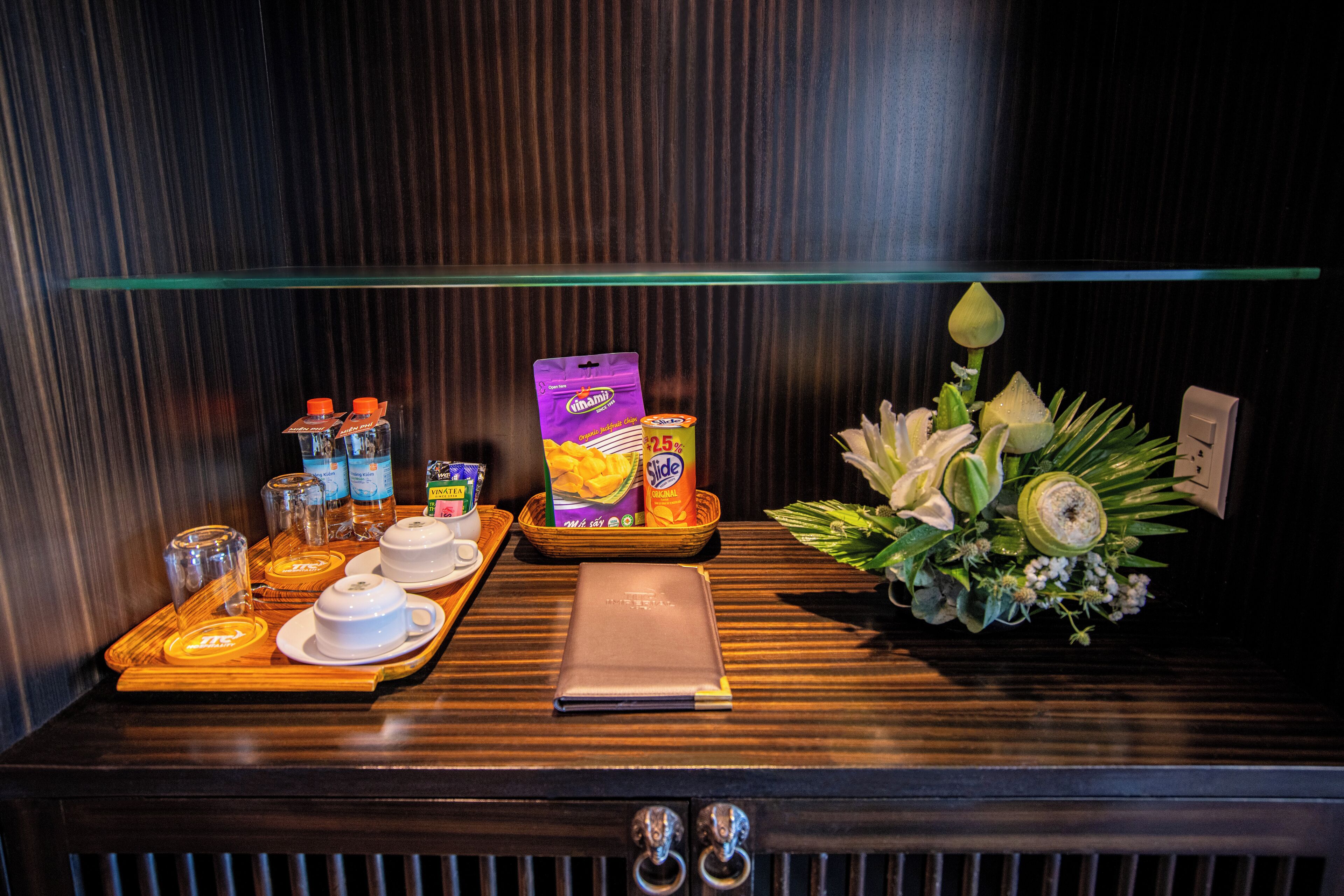 A wooden counter with a tray containing a laptop, a box of snacks, a bottle of water, and a small bouquet of flowers.