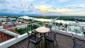 A balcony with a table and chairs overlooking a cityscape and river. - TTC Imperial Hotel (Hue)