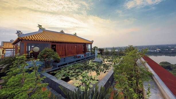 A traditional building with a tiled roof, surrounded by a water garden with lotus plants. - TTC Imperial Hotel (Hue)