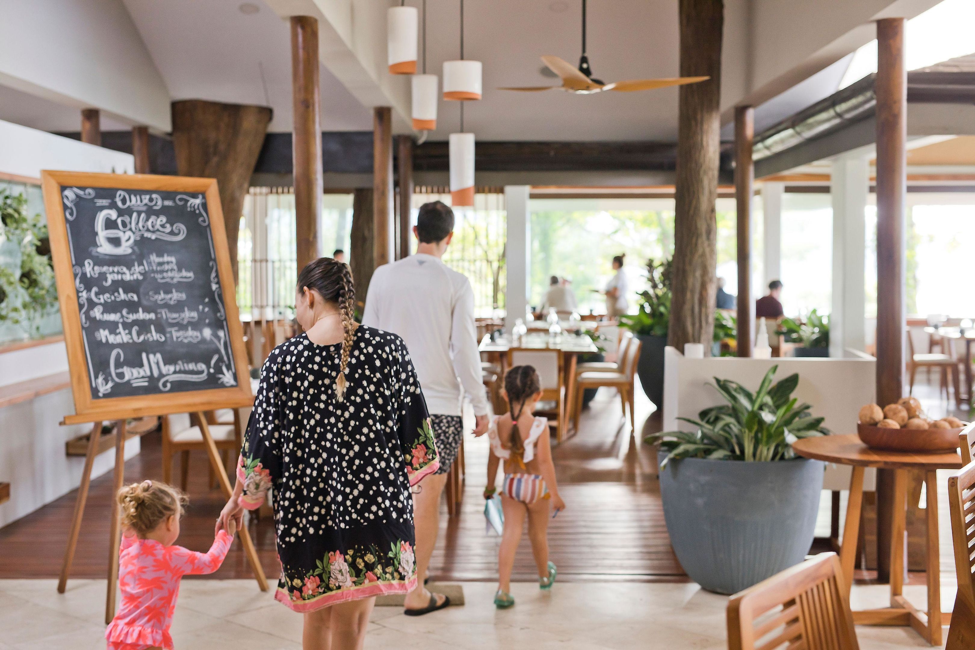 A spacious indoor area with wooden flooring, a chalkboard menu, and a large potted plant.