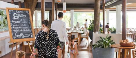 A spacious indoor area with wooden flooring, a chalkboard menu, and a large potted plant.