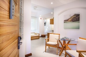 A modern hotel room with a wooden wall, a glass table with chairs, a bed with a wooden headboard, and a painting on the wall.