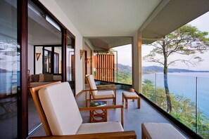 A balcony with a view of a body of water and greenery, furnished with chairs and a small table. - Arenas Del Mar Beachfront & Rainforest Member of the Cayuga Collection (Quepos)