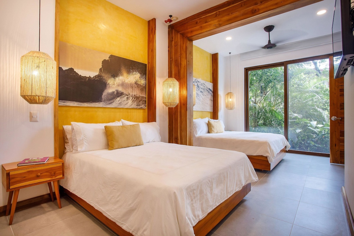 A hotel room with two beds, wooden beams, a large window with a view of greenery, and a painting on the wall.