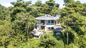 A two-story house surrounded by dense forest, with a thatched-roof structure and a large glass window. - Arenas Del Mar Beachfront & Rainforest Member of the Cayuga Collection (Quepos)