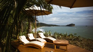 A wooden deck with lounge chairs and a table, overlooking a beach with clear waters and a small island in the distance. - Arenas Del Mar Beachfront & Rainforest Member of the Cayuga Collection (Quepos)