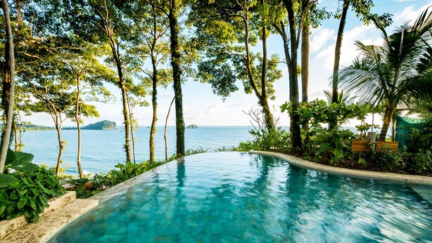 A clear blue pool surrounded by lush greenery and a view of the sea. - Arenas Del Mar Beachfront & Rainforest Member of the Cayuga Collection (Quepos)