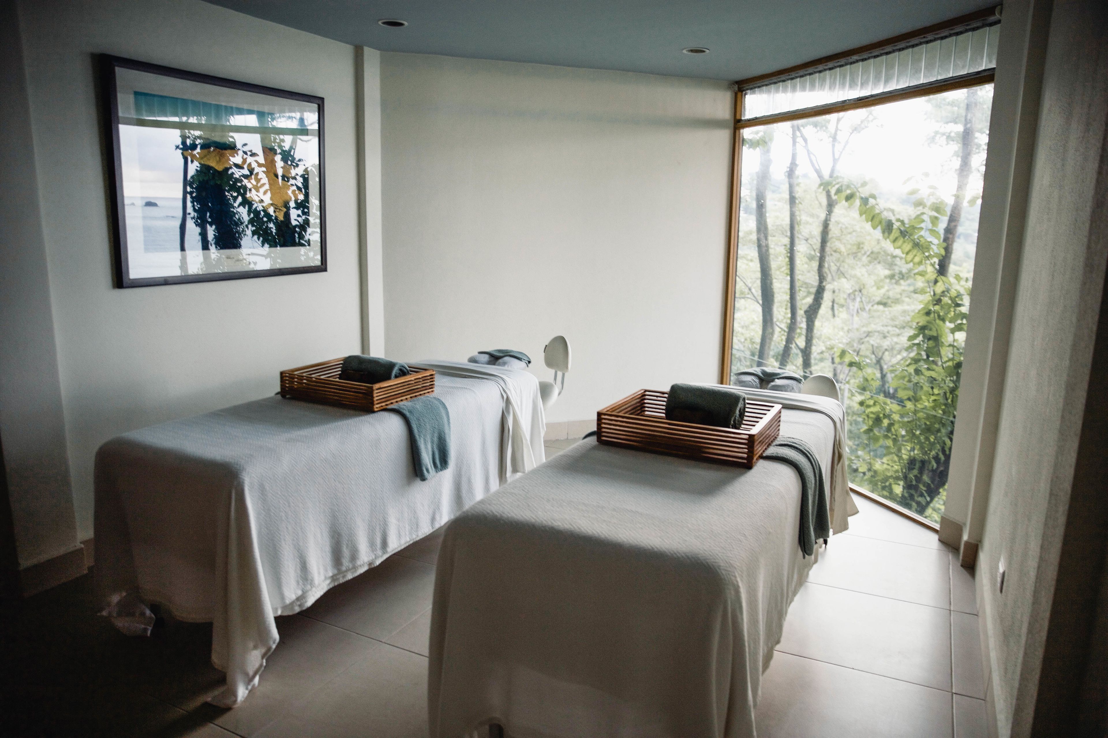 Una habitación con dos camas, un cuadro en la pared y un gran ventanal con vista a los árboles.