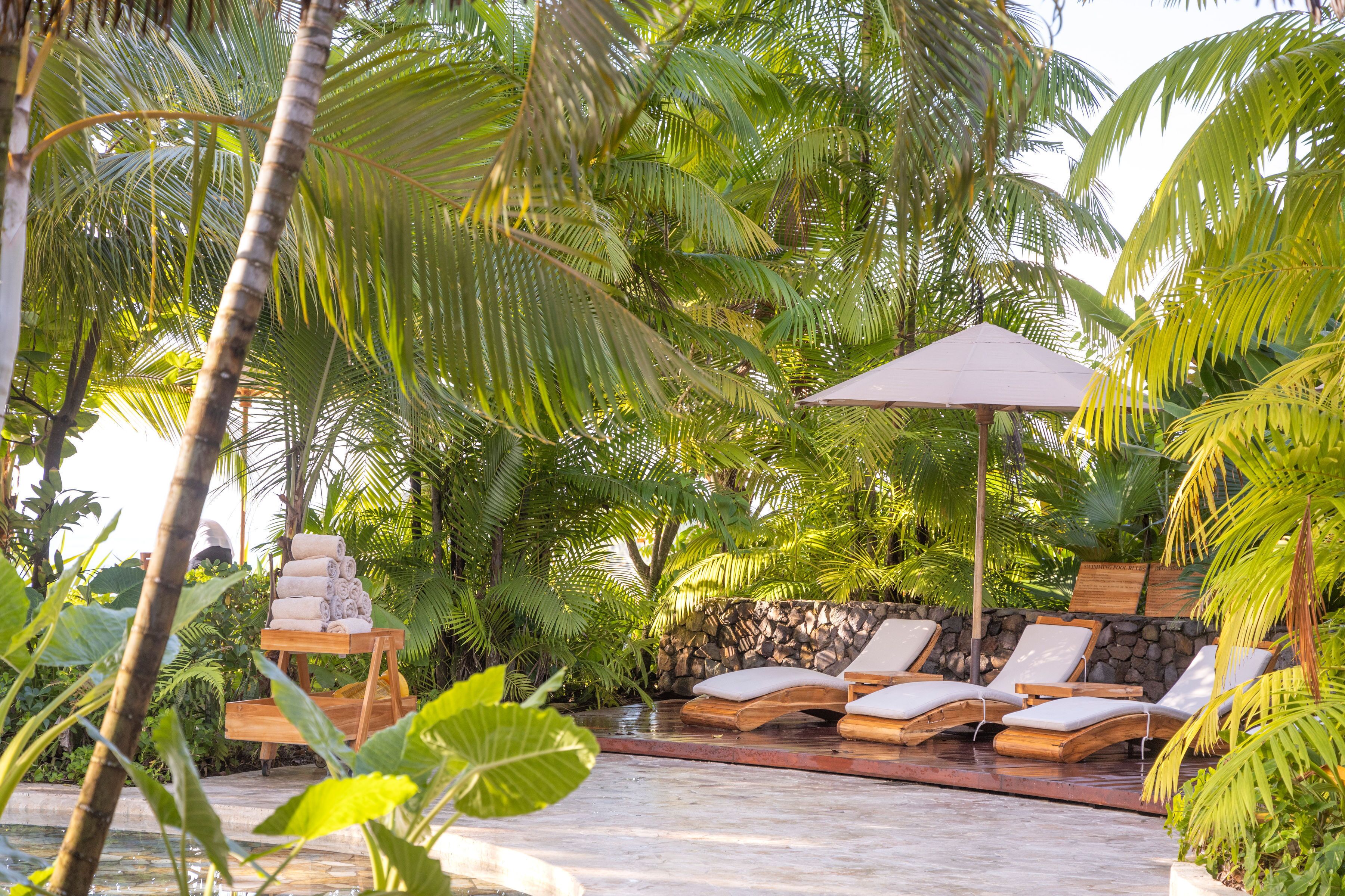 A poolside area with lounge chairs, a table with towels, and a stone wall.