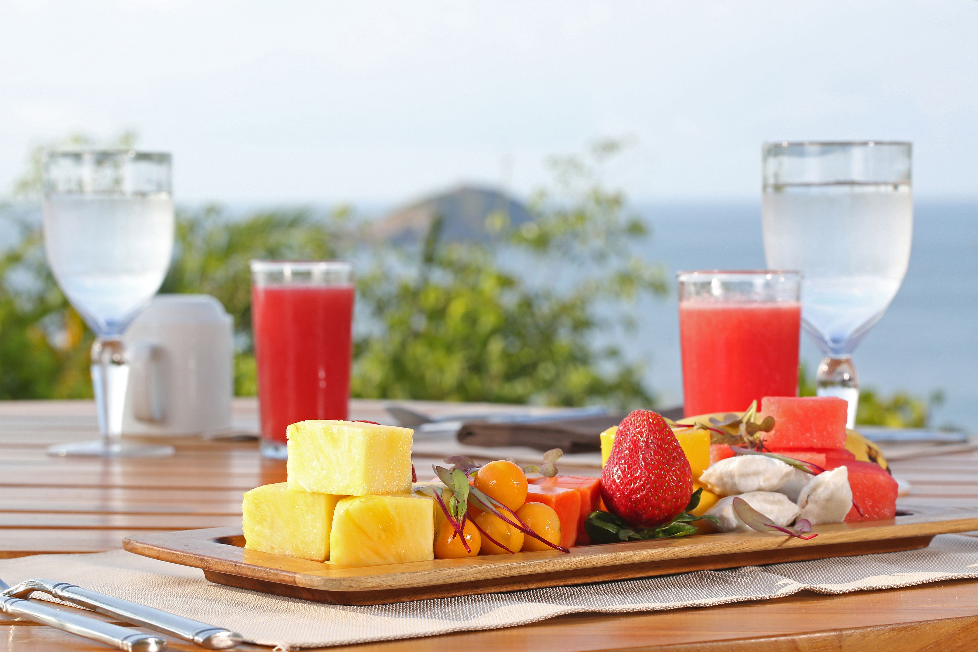 A wooden table with a fruit platter, two glasses of water, and a white pitcher.