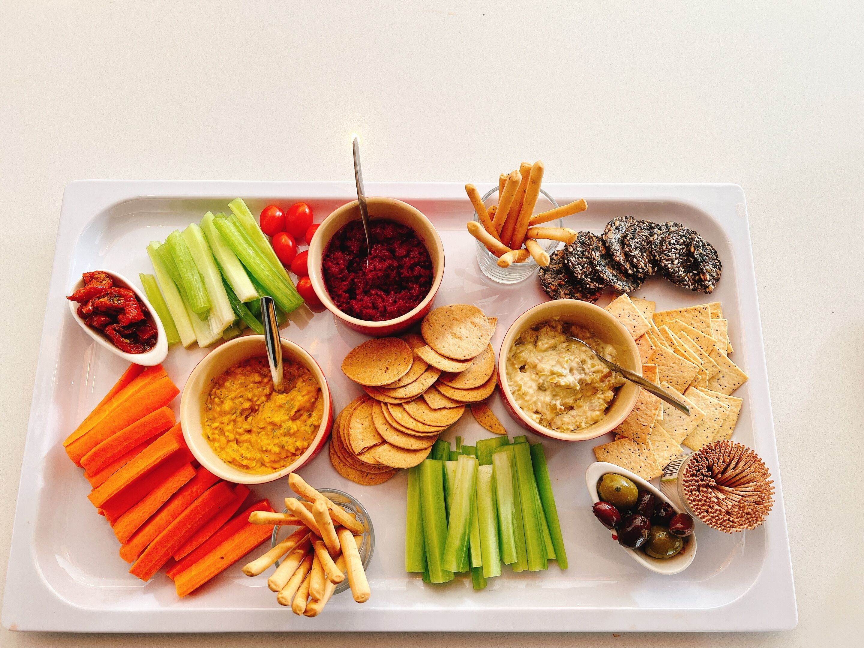 Una bandeja con diversos bocadillos, como salsas, verduras y galletas.