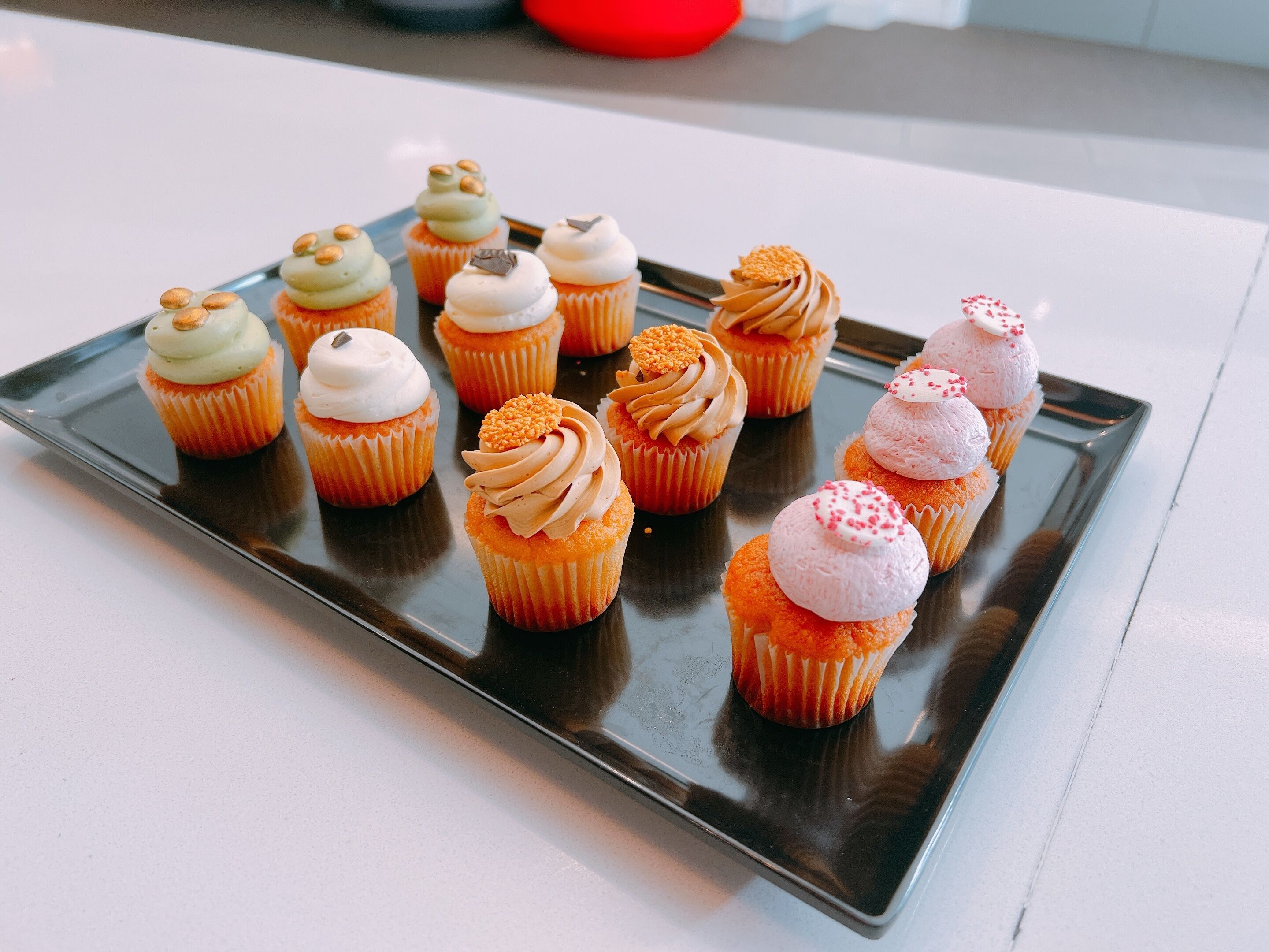 Un plateau rempli de cupcakes de différentes sortes, chacun agrémenté d’un glaçage différent.