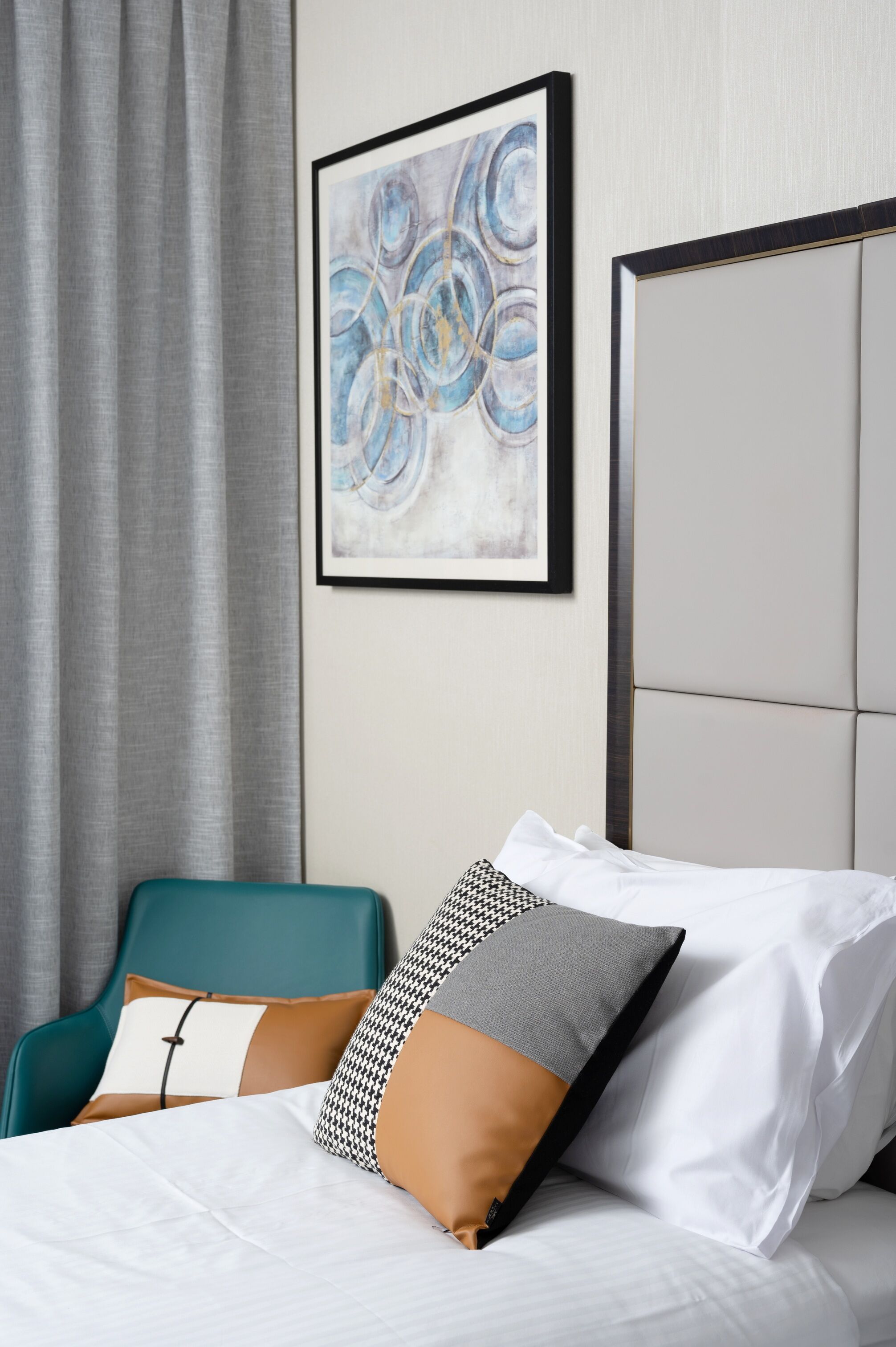 Una cama bien hecha con sábanas blancas y una silla turquesa con cojines estampados.