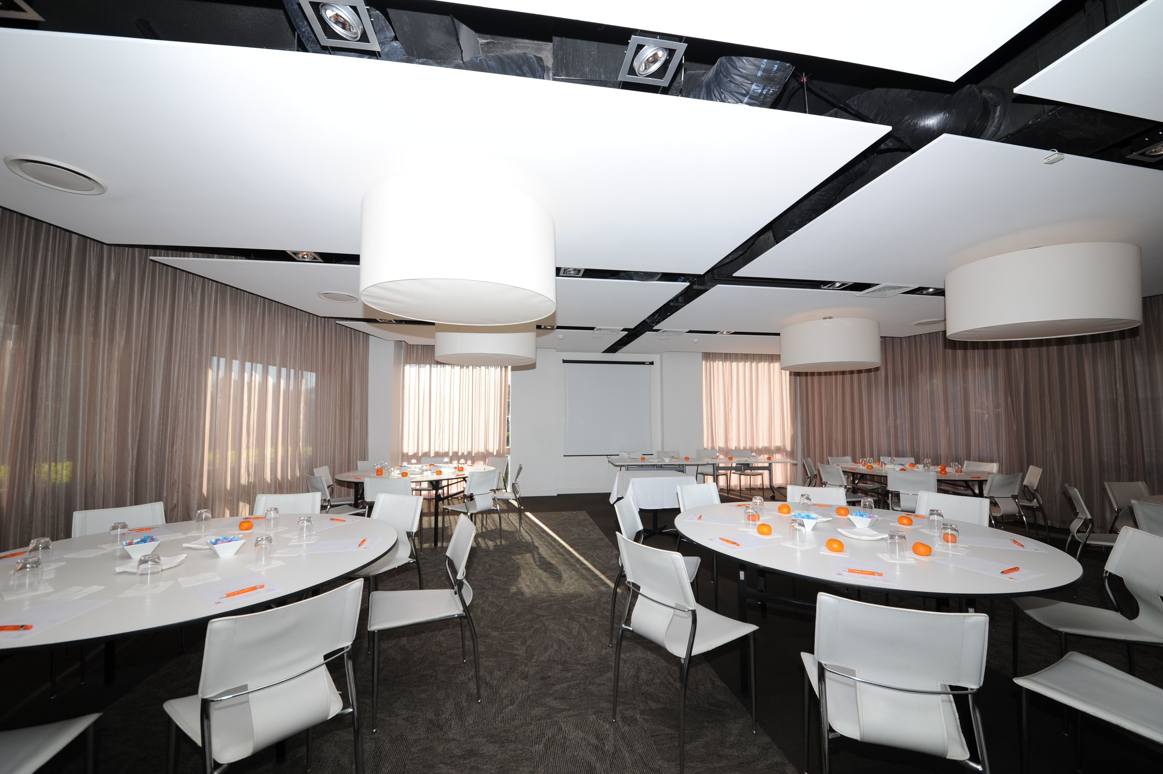 A conference room with round tables, white chairs, and large ceiling lights.