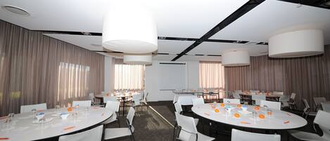 A conference room with round tables, white chairs, and large ceiling lights.