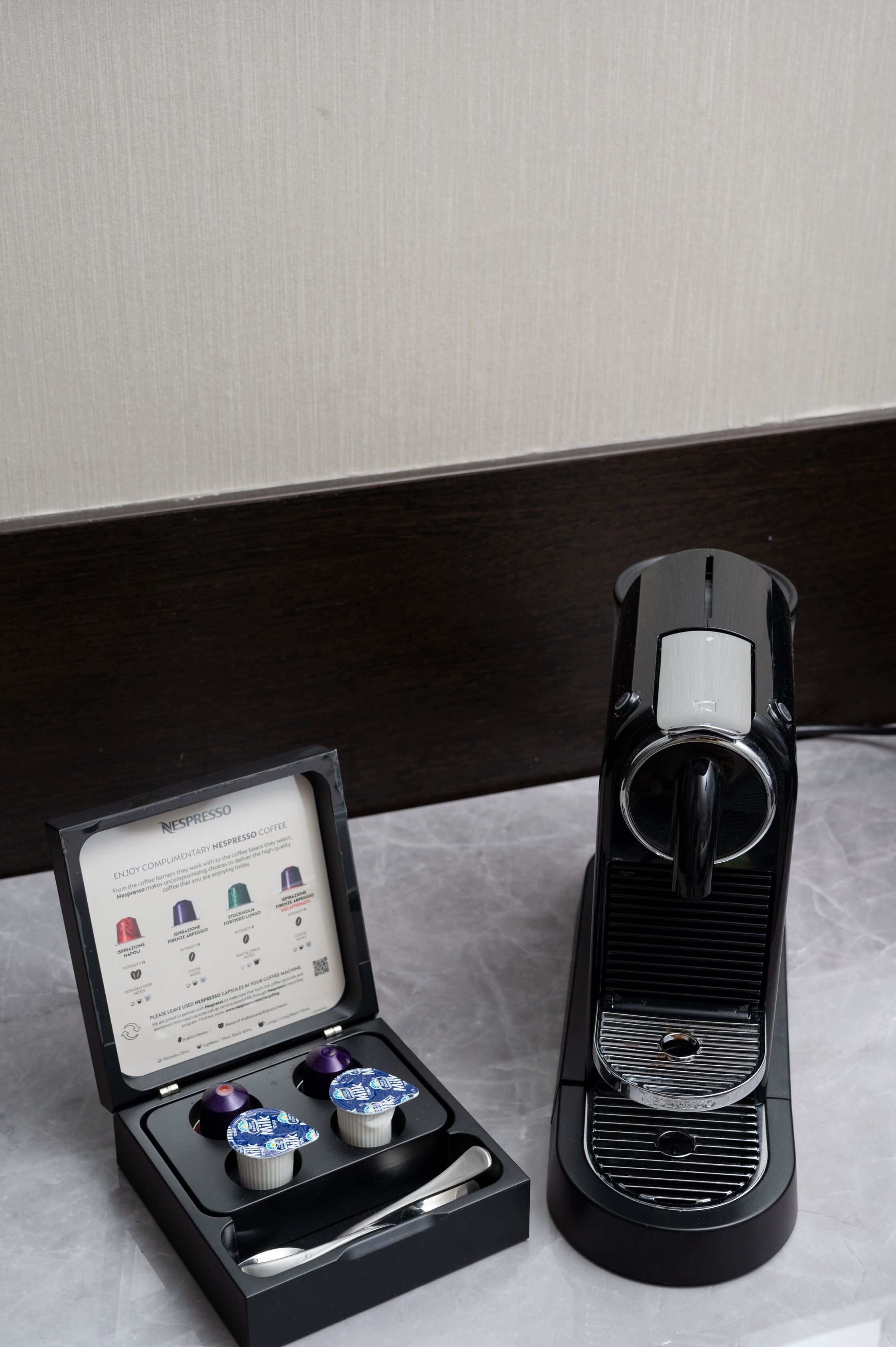 A Nespresso coffee machine with a box containing two capsules and a spoon.