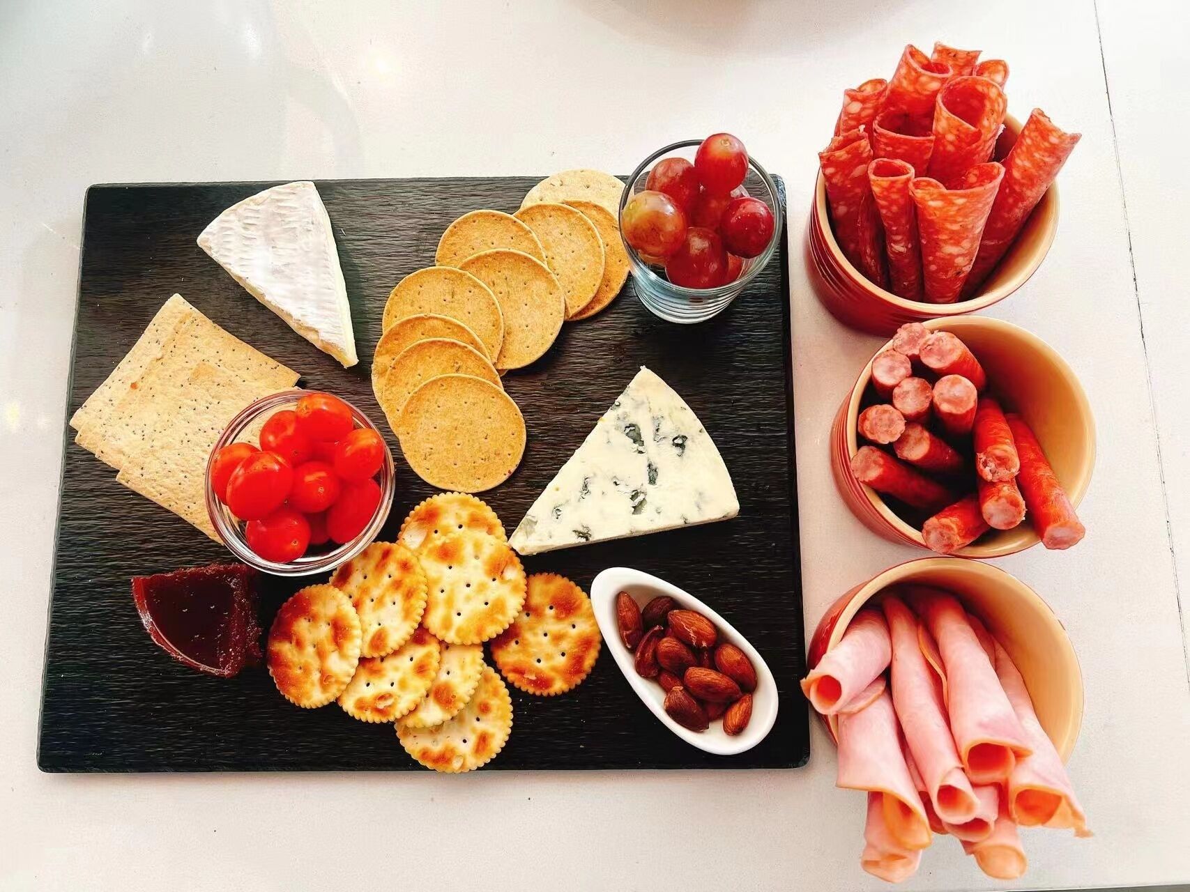Een plank met verschillende kazen, crackers, druiven en vleeswaren.