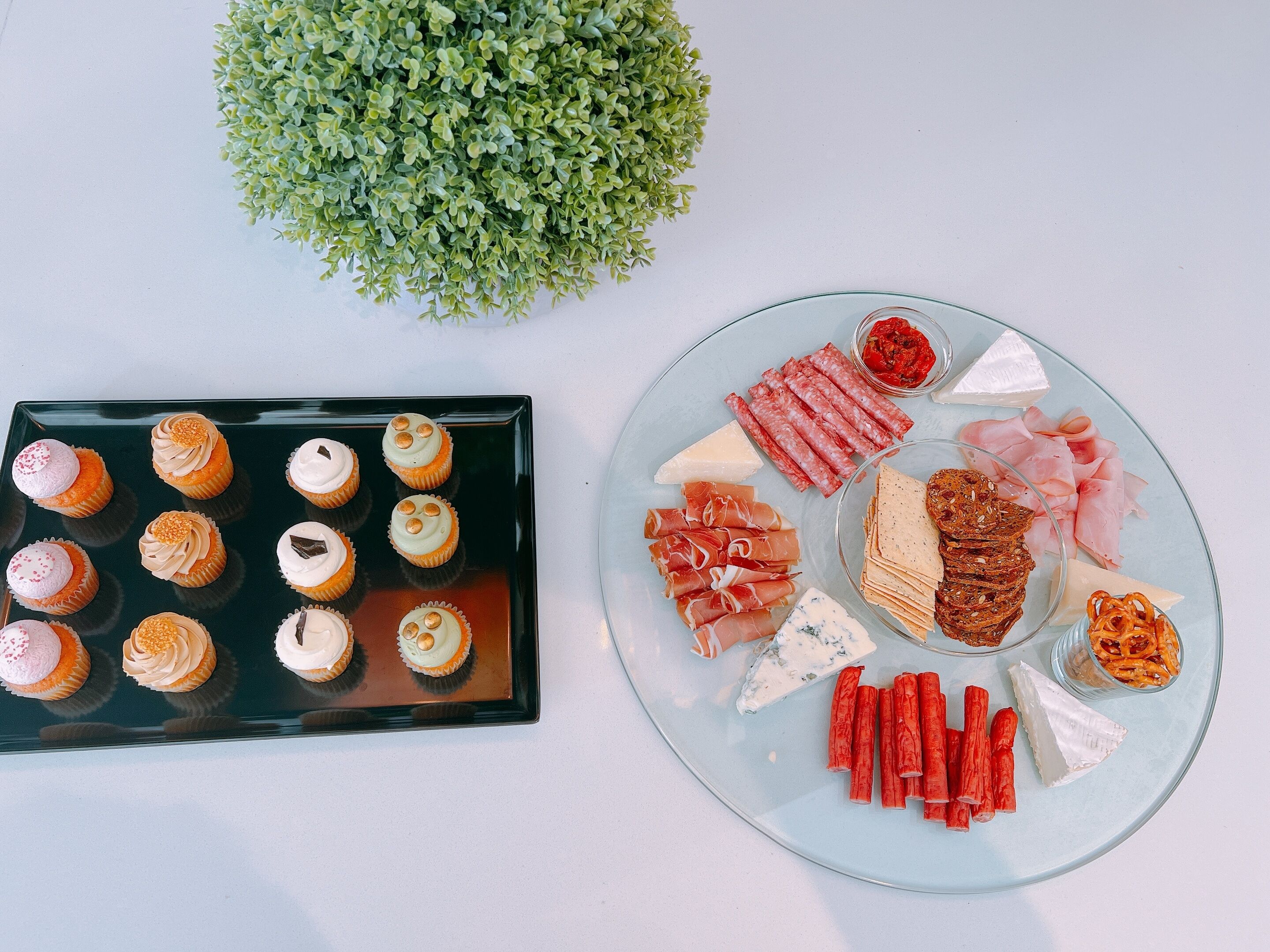 Un tavolo imbandito con diversi cibi tra cui cupcake, formaggi, salumi e cracker.