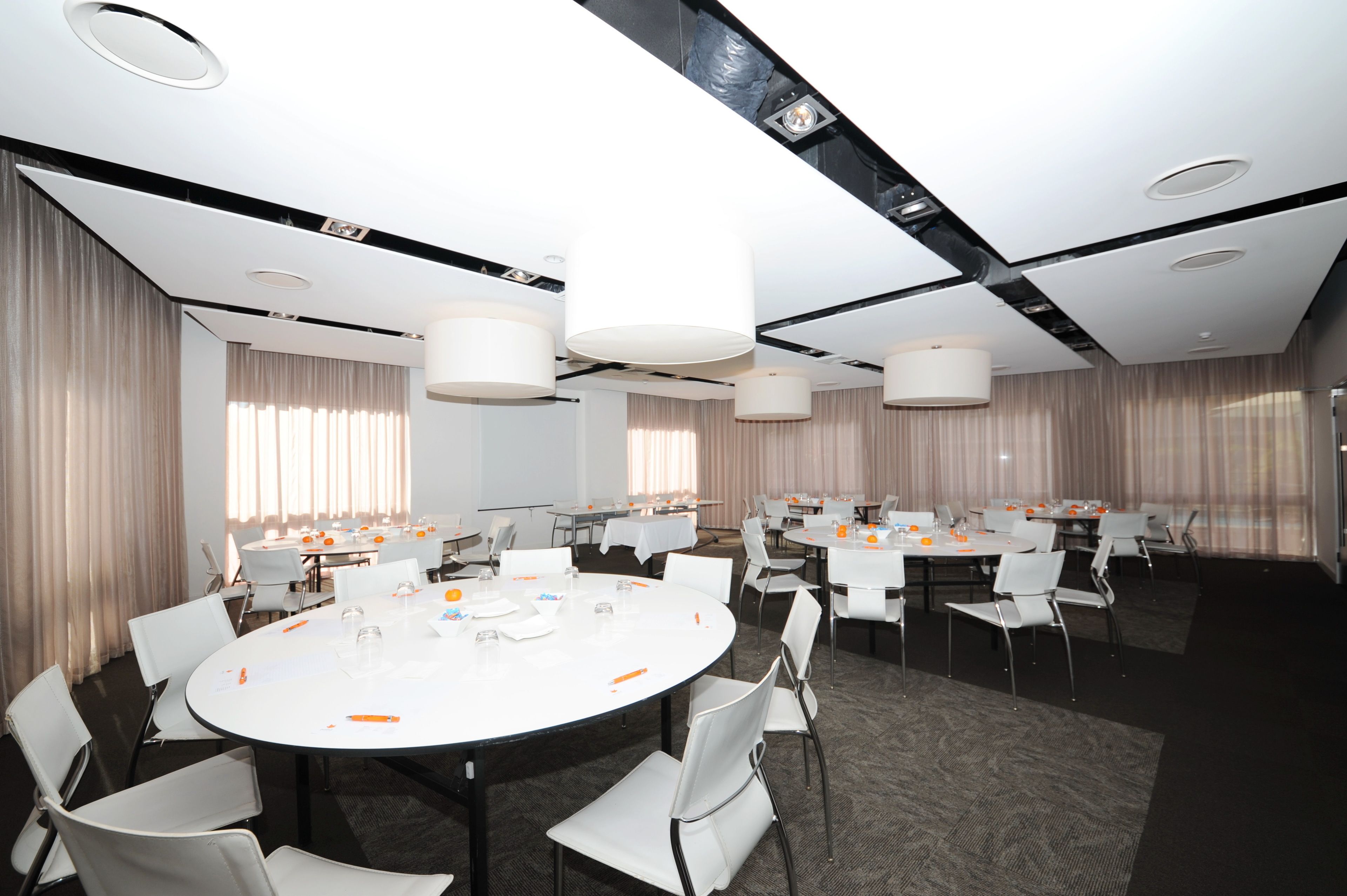 A conference room with round tables, white chairs, and large pendant lights.