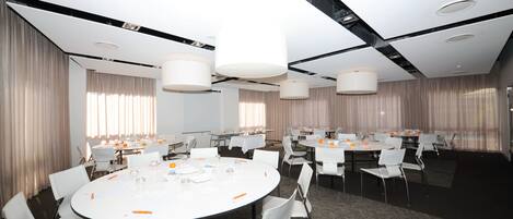 A conference room with round tables, white chairs, and large pendant lights.