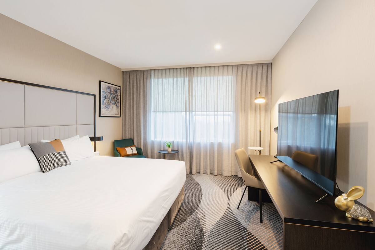 A hotel room with a large bed, a desk, a television, and a window with curtains.