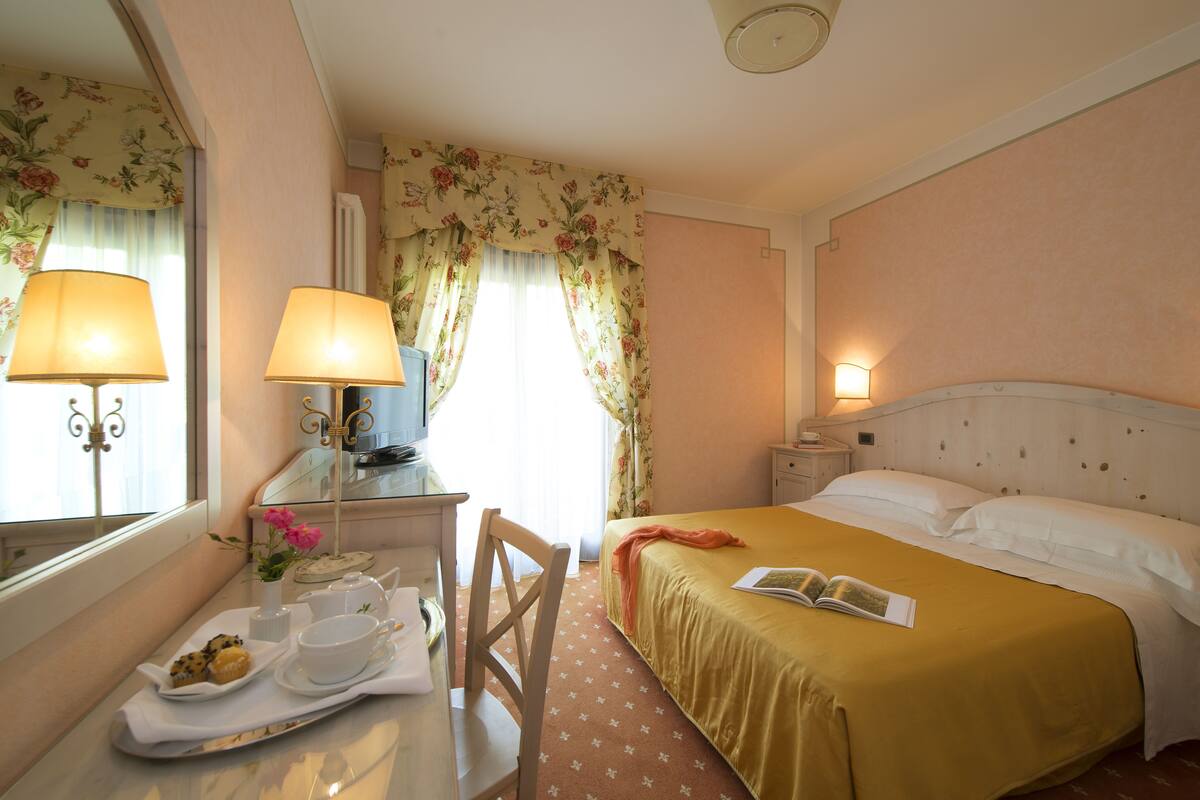 Een hotelkamer met een bed, nachtkastje, lamp en een raam met gordijnen.