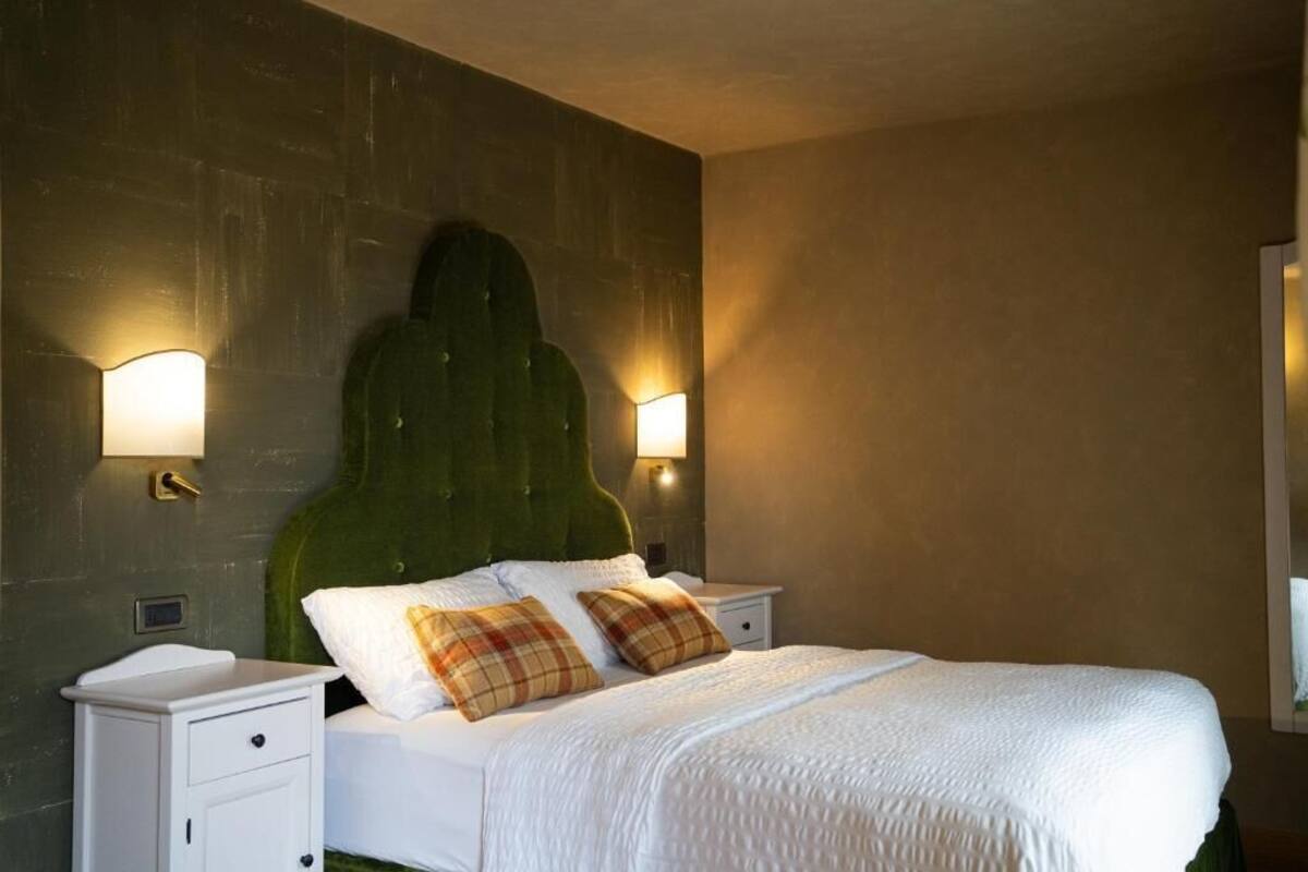 Een slaapkamer met een groen bekleden hoofdeinde, twee nachtkastjes, een wit bed met een geribbeld witte dekbedovertrek en twee ruitkussens.