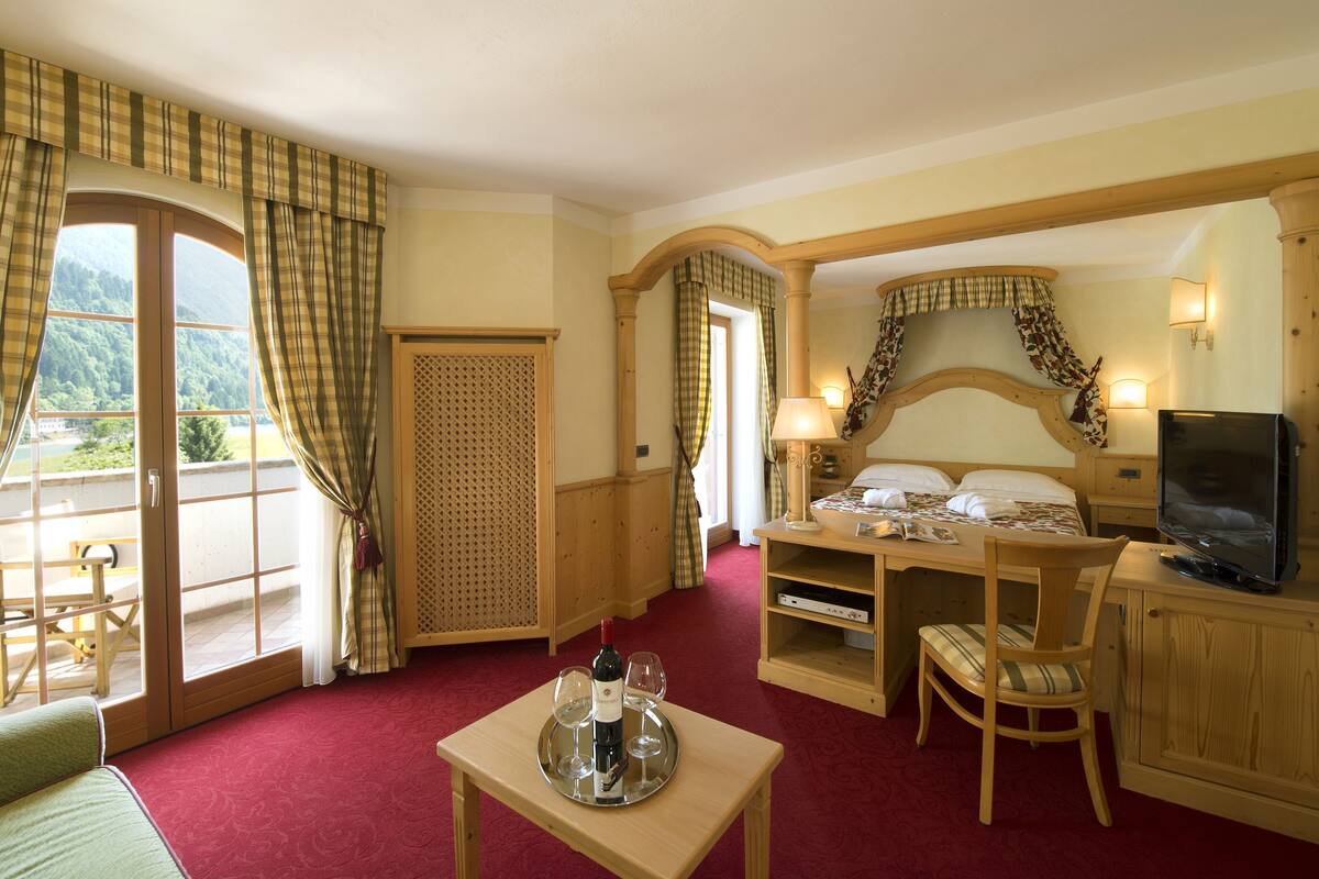 Een hotelkamer met een bed, een televisie, een eettafel met een fles wijn, en uitzicht op de omgeving.