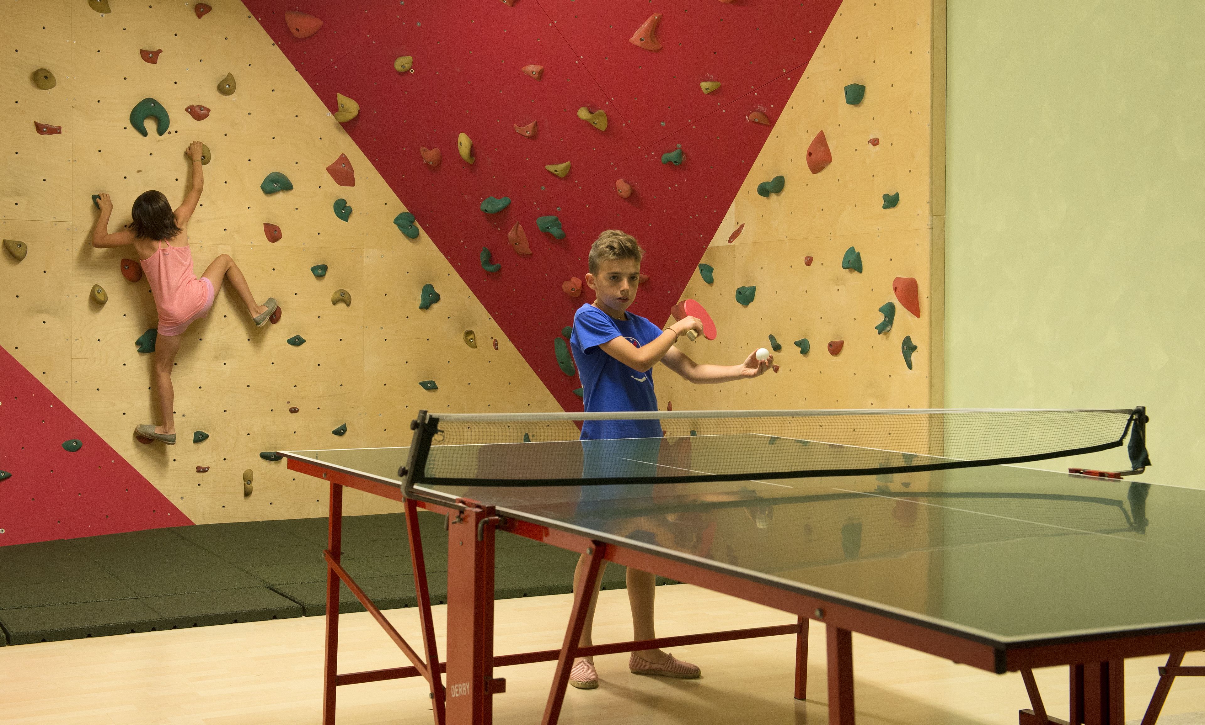 Una parete da arrampicata con diverse asce e un tavolo da ping pong in primo piano.