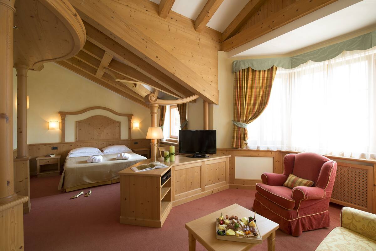 Een hotelkamer met een houten plafond, een bed, een televisie, een rode fauteuil en een klein tafeltje met fruit.