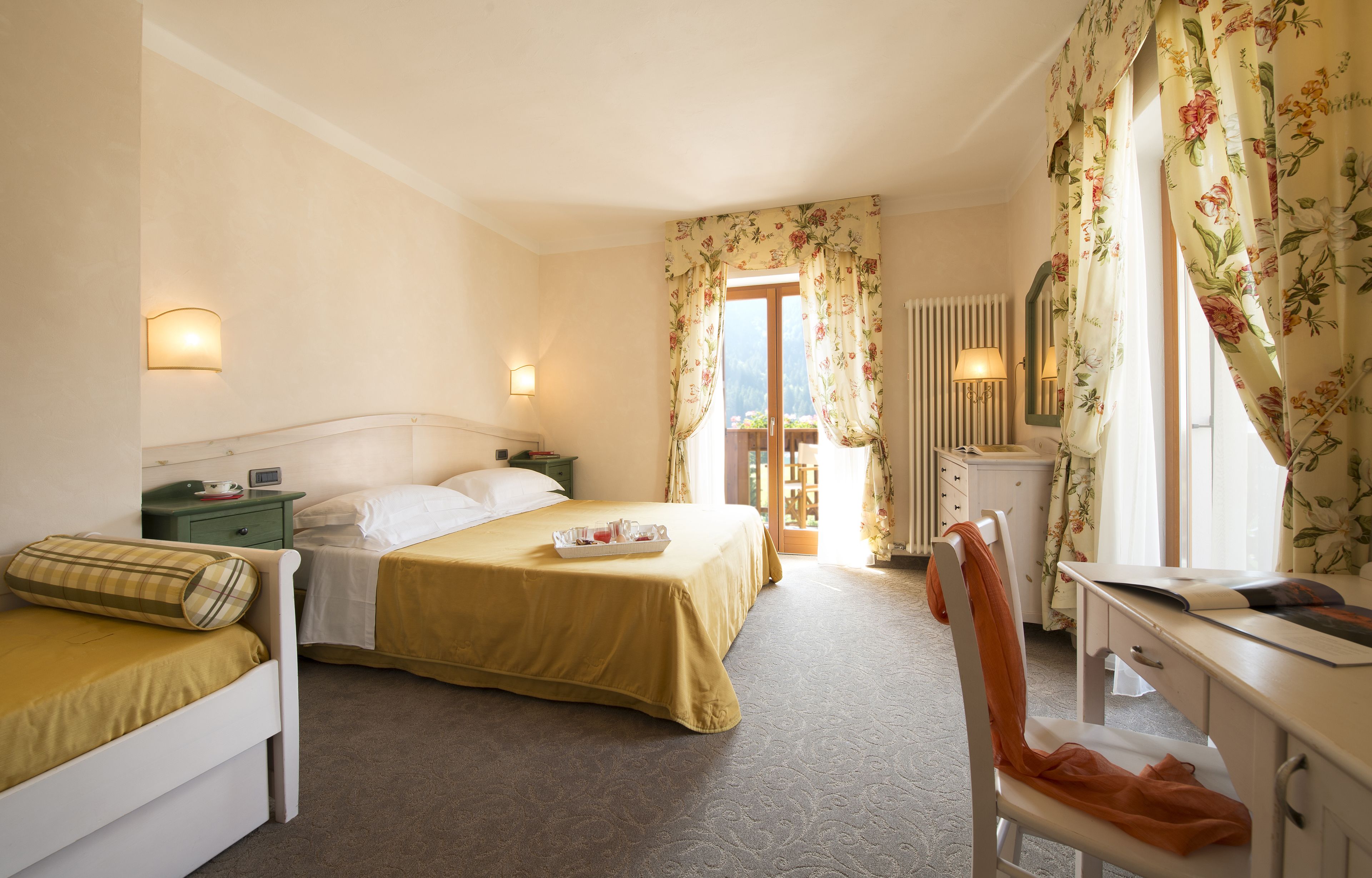 Habitación de hotel con dos camas, un escritorio, una silla y una ventana con cortinas florales.