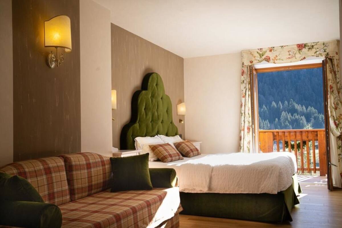 Een slaapkamer met een bed, een slaapbank, een hoofdeinde en uitzicht op bergen door een raam.