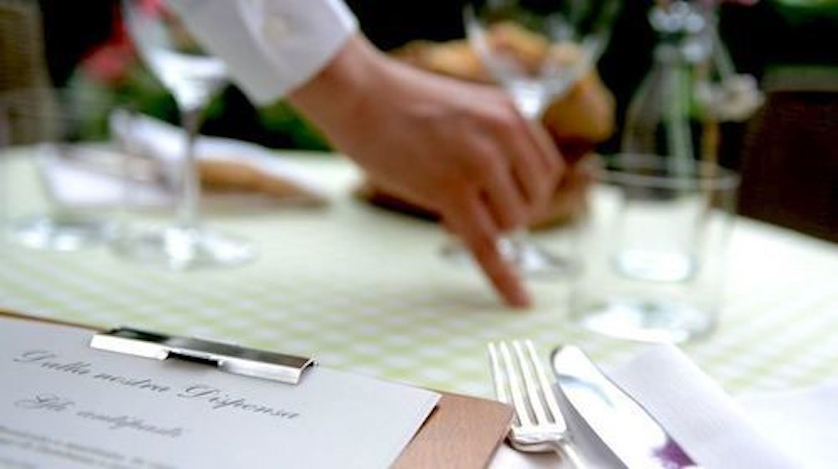 Een eettafel met een menukaart, een pen, een vork en een glas.