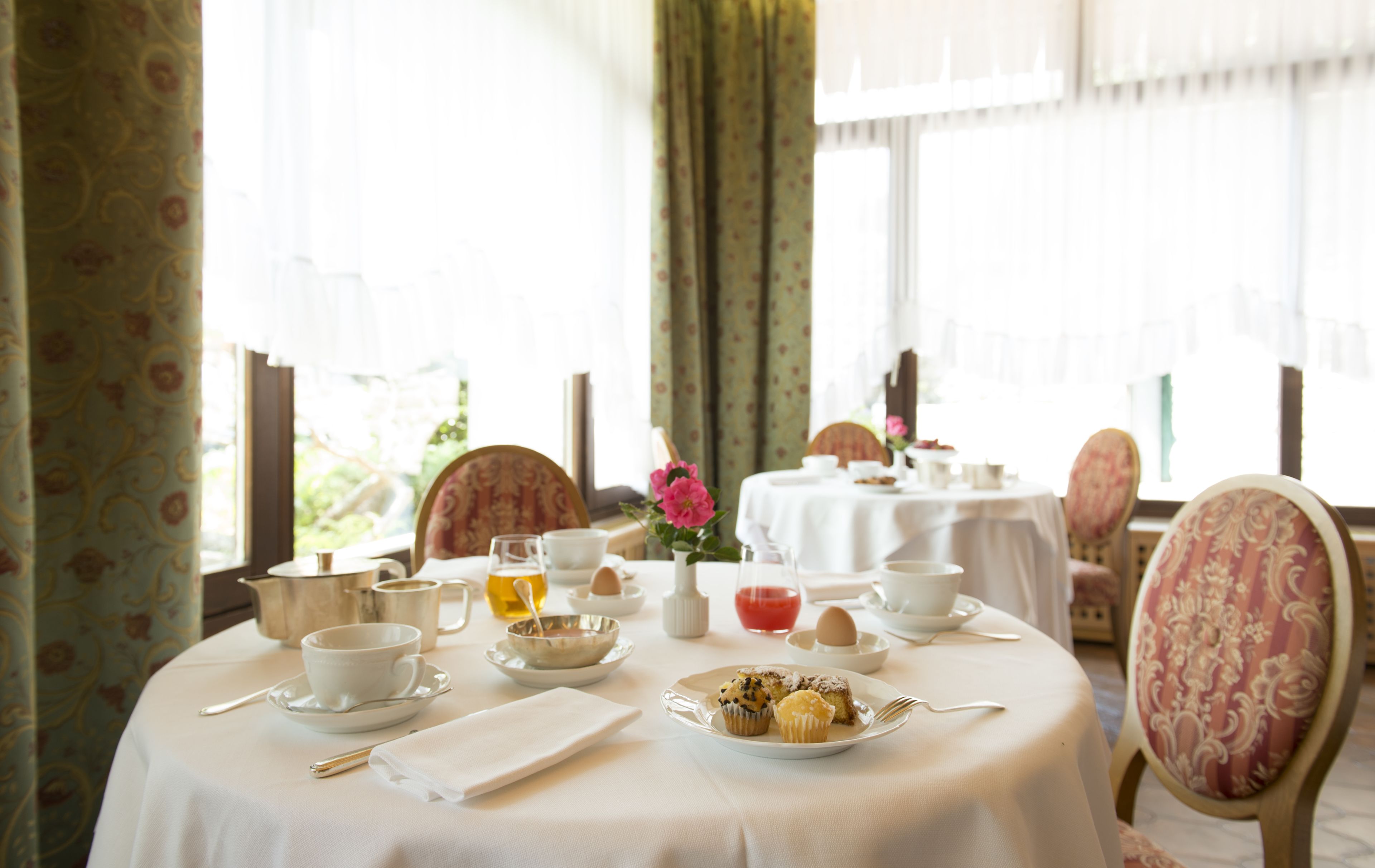 A dining table set with tea cups, saucers, a plate with pastries, and a teapot.