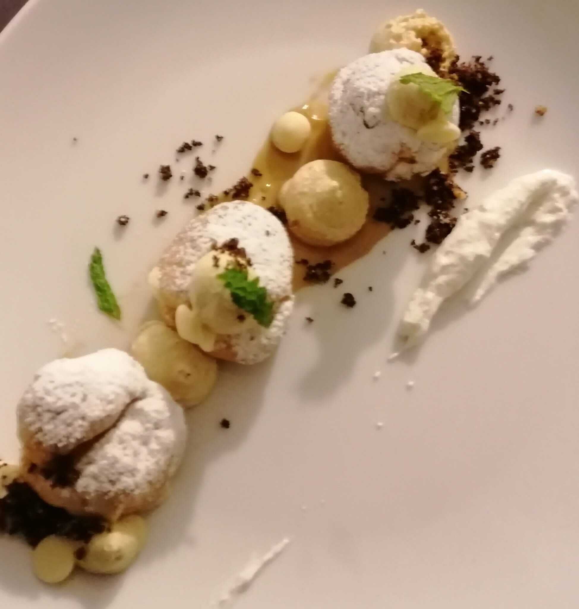 En dessert som består av olika delar, bland annat sfärer, en sås och pudersocker.