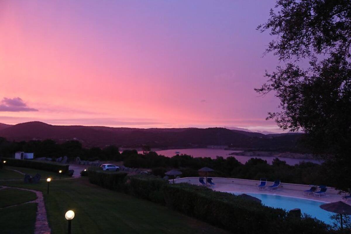 Ein Poolbereich mit Liegestühlen, ein Steinhaus und ein See im Abenddämmerung.