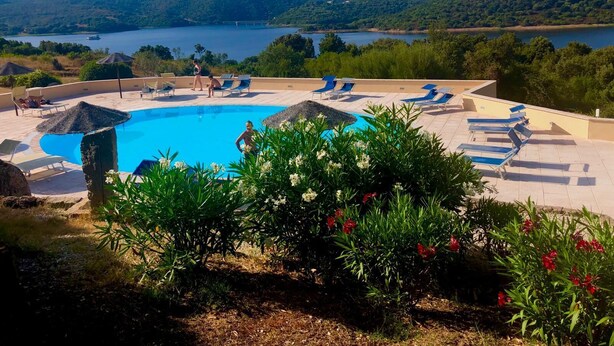 Ein Poolbereich mit Liegestühlen und Blick auf einen See und Hügel.