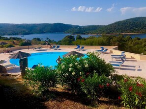 A pool area with lounge chairs and a view of a lake and hills. - Hotel Relais Valkarana (Sant'Antonio di Gallura)